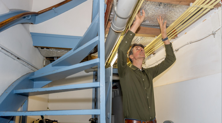 Op de foto is een man bezig met het isoleren van zijn plafond in de gang van zijn huis.